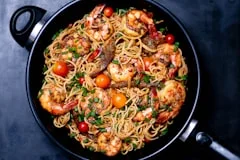 Shrimp pasta with cherry tomatoes served in a black pan